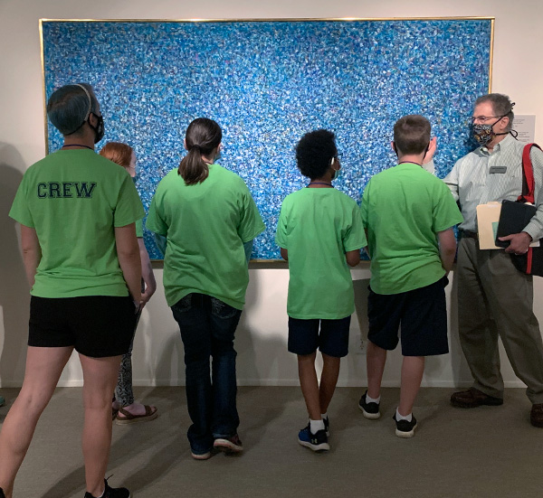 Students in matching shirts watch a docent give a tour.